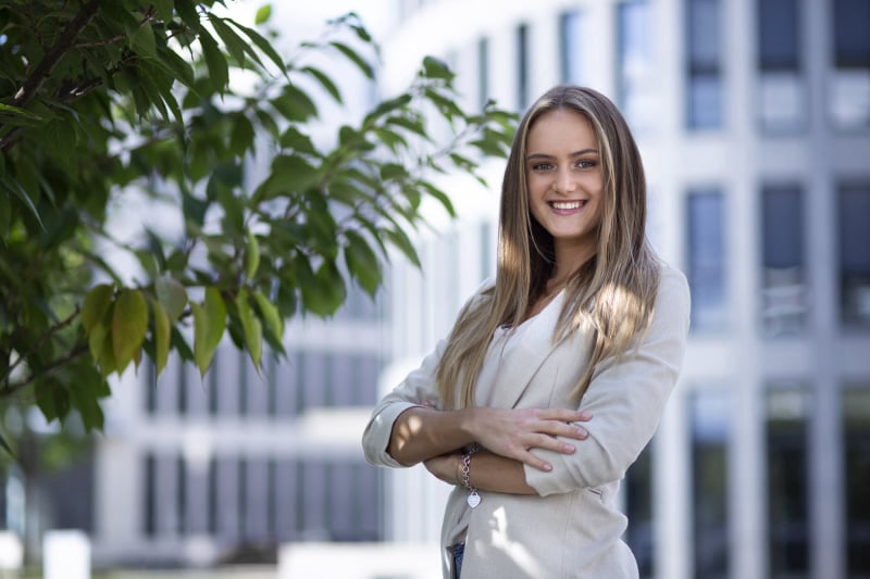 Bewerbungsfoto einer Frau im hellen Blazer vor einer modernen Fassade